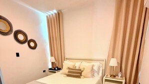 A neatly made bed with a white headboard, two bedside tables with lamps, and a wooden floor. - Carribbean Oasis Cozy 1-bedroom apartment in delightful Punta Cana with AC (Punta Cana)