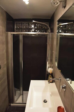A modern bathroom with a glass-enclosed shower, a white sink, and a large mirror.