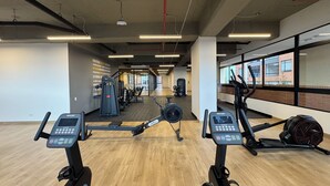 Ein Fitnessstudio mit Cardiogeräten, Gewichten und einem großen Fenster mit Blick auf Gebäude.