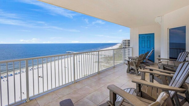 A balcony with a view of the beach and ocean, a blue door, and several chairs. - 🏖️ Admirals Quarters 1201 | 4BR Corner Condo | Gulf + Bay Views + Pool (Orange Beach)