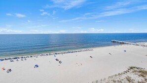 A beach with a pier extending into the water, sandy beach, and clear skies. - 🏖️ Admirals Quarters 1201 | 4BR Corner Condo | Gulf + Bay Views + Pool (Orange Beach)
