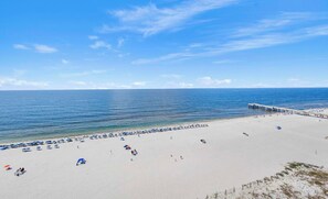 Ein Strand mit einem Steg, der sich ins Wasser erstreckt, feinem Sand und blauem Himmel.