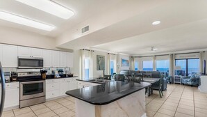 A modern kitchen with white cabinets, a black countertop island, stainless steel appliances, and a dining area with a view. - 🏖️ Admirals Quarters 1201 | 4BR Corner Condo | Gulf + Bay Views + Pool (Orange Beach)