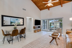 A spacious living room with a dining area, a flat-screen TV, and a balcony with a view. - Villa Sanibel 3D | Pelican Perch Loft | Spacious Coastal Retreat (Sanibel)