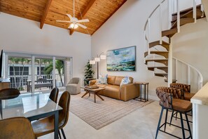 A spacious living area with a glass dining table, leather sofa, and a spiral staircase. - Villa Sanibel 3D | Pelican Perch Loft | Spacious Coastal Retreat (Sanibel)