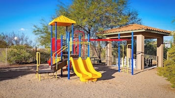 A playground with a slide, climbing structures, and a covered seating area.