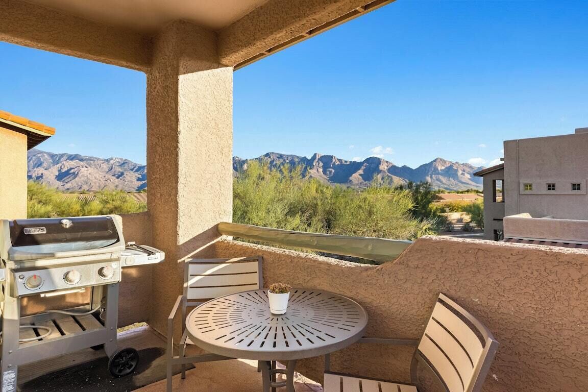 Un balcon avec un barbecue, une table, des chaises et une vue sur les montagnes.