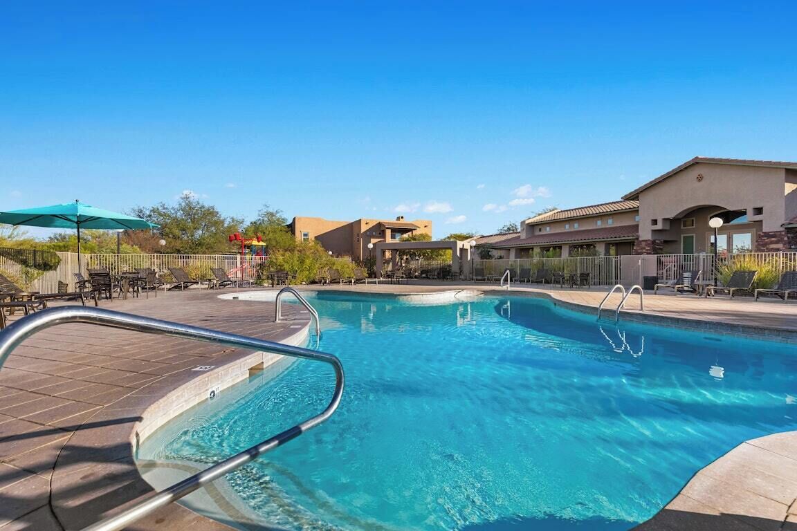 A swimming pool with a metal ladder, lounge chairs, and a covered area with an umbrella.