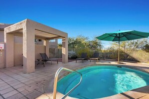 A swimming pool with a sunshade, lounge chairs, and a covered seating area.