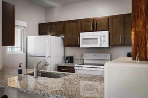 A kitchen with granite countertops, a white refrigerator, a microwave, and a stove.