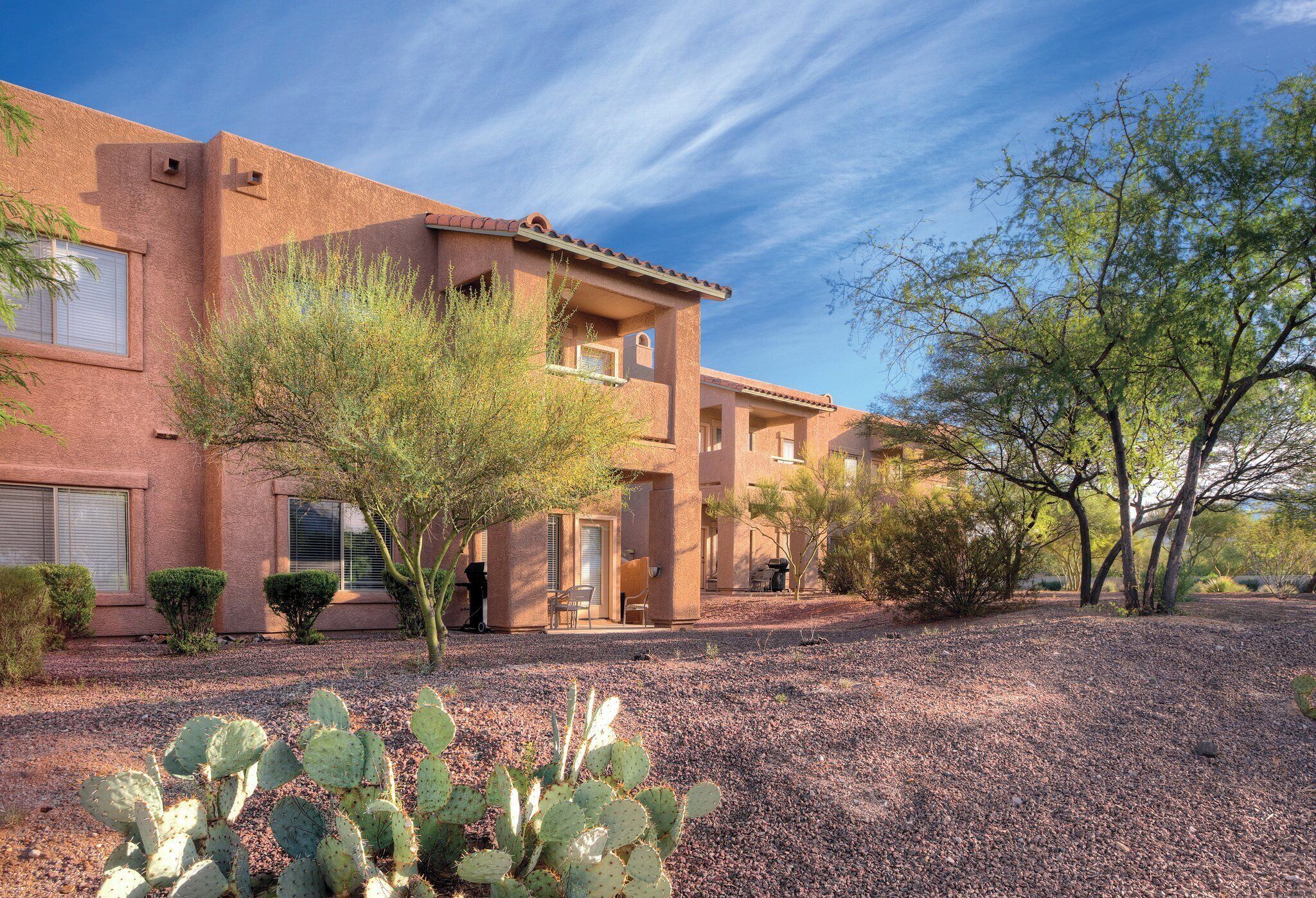 Un immeuble à plusieurs étages, doté d’un toit plat, d’une allée en gravier et d’un cactus en premier plan.