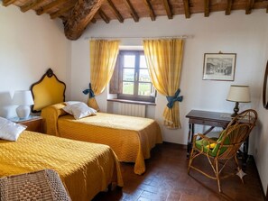 Ein Zimmer mit zwei Betten, einem Sessel, einem Tisch und einem Fenster mit Vorhängen.