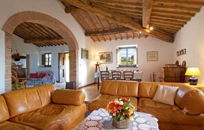 Uma sala de estar aconchegante com um sofá de couro, uma área de jantar com mesa e cadeiras, e uma cozinha visível por um arco.