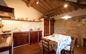 Uma cozinha rústica com armários de madeira, uma parede de pedra e uma mesa posta para refeições.
