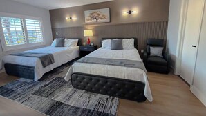 Camera d'albergo con due letti, un comodino, una lampada, una sedia e una finestra con persiane.