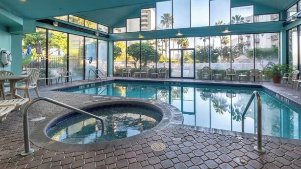 Una piscina interna con una vasca idromassaggio, circondata da pareti di vetro e area relax all'aperto.