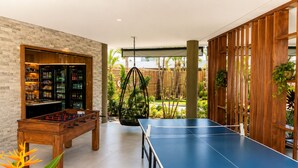 Une pièce équipée d’un baby-foot, d’une table de ping-pong et d’un bar avec des étagères remplies de bouteilles.