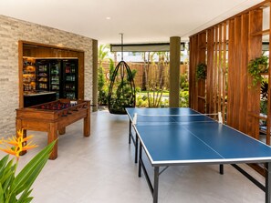 A room with a foosball table, ping pong table, and a bar area with shelves of bottles. - Spacious 1-bedroom apartment with AC in perfect Ipojuca (Ipojuca)
