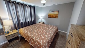 A bedroom with a bed, a nightstand, a lamp, a painting, and a wooden dresser. - -Cheerful 3 bed home--inside COMPLETELY renovated! (Hays)