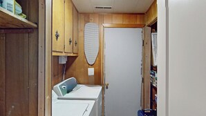 A laundry room with a washing machine, dryer, ironing board, and a door leading to a storage area. - -Cheerful 3 bed home--inside COMPLETELY renovated! (Hays)