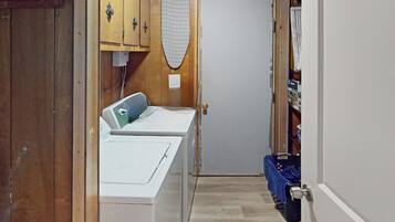 Une buanderie équipée d’un lave-linge, d’un sèche-linge, d’une planche à repasser et d’une porte donnant accès à un espace de rangement.