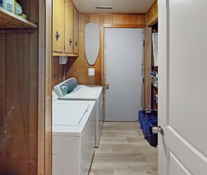 Une buanderie équipée d’un lave-linge, d’un sèche-linge, d’une planche à repasser et d’une porte donnant accès à un espace de rangement.