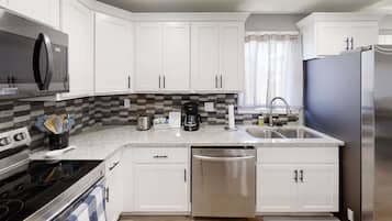 Una cocina moderna con gabinetes blancos, un refrigerador de acero inoxidable, un microondas y un lavavajillas.