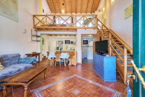A spacious living area with a wooden staircase, a dining table, and a kitchen in the background. - Casa Dos Irmaos in the Valley of the Orange Trees (Silves)