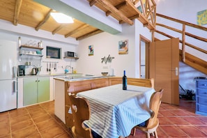 A kitchen with wooden beams, a dining table with a striped tablecloth, and a bottle of wine. - Casa Dos Irmaos in the Valley of the Orange Trees (Silves)