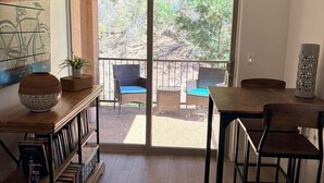 Een kamer met houten vloer, een boekenkast, een eettafel met stoelen, en een grote schuifdeur naar een terras buiten met stoelen en een tafel.