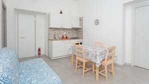 Quarto compacto com cama, mesa de jantar com cadeiras, cozinha compacta e porta branca.