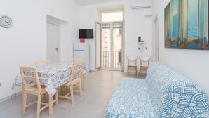 Um quarto com uma mesa de jantar, cadeiras, um sofá, uma televisão e uma porta que dá para uma varanda externa.