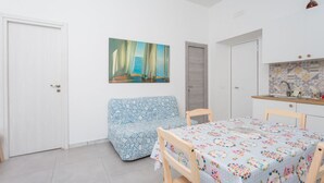 Um quarto com sofá, mesa de jantar, um quadro e uma área de cozinha.