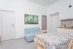 Ein Zimmer mit einer Couch, einem Esstisch, einem Gemälde und einer Küchenzeile.