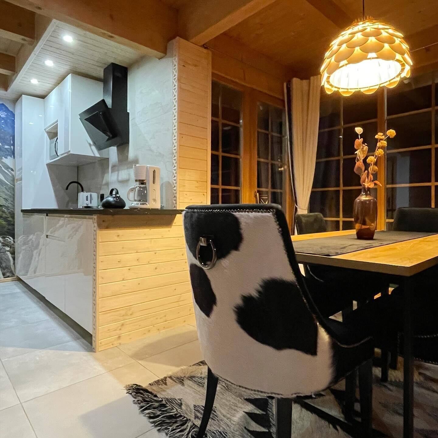 Un coin repas avec une table en bois, une chaise aux motifs noir et blanc, un vase avec des fleurs et une suspension.