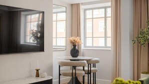 A modern living room with a flat-screen TV, a round table with chairs, a vase with dried plants, and a potted plant. - The Folio Collection (London)