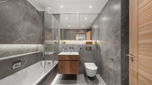 A modern bathroom with a bathtub, a toilet, and a vanity. - The Folio Collection (London)