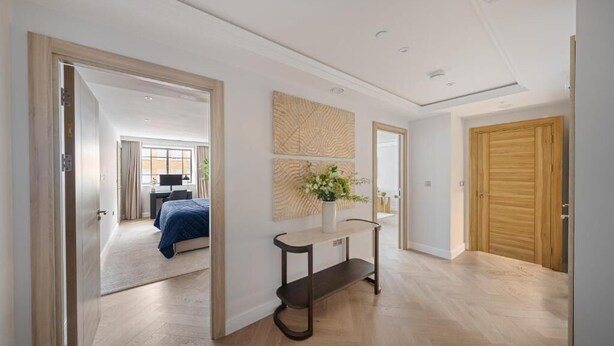 A modern interior with a wooden floor, a console table with a vase, and a large mirror. - The Folio Collection (London)