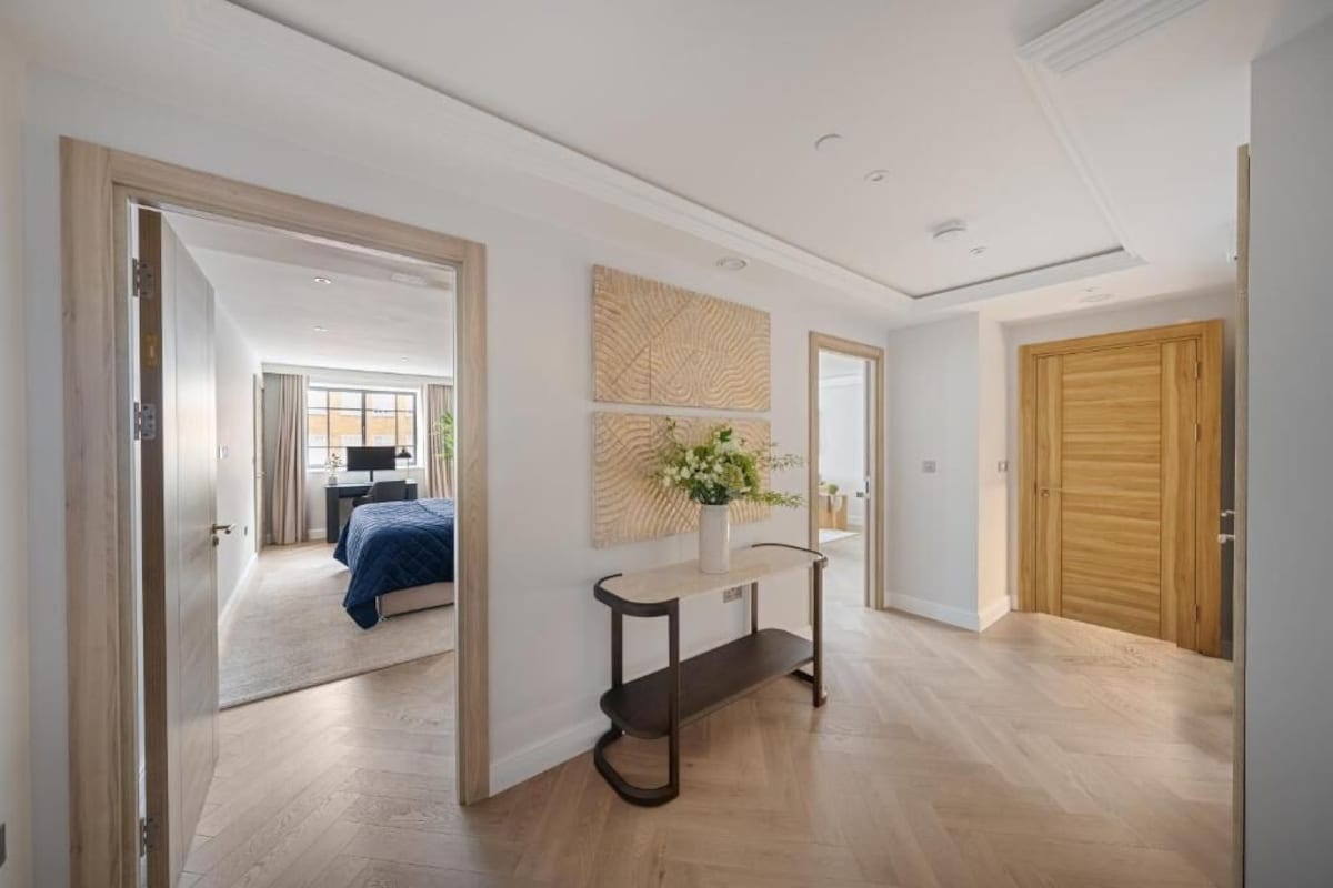 A modern interior with a wooden floor, a console table with a vase, and a large mirror.