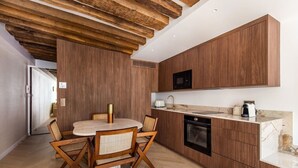 A modern kitchen with wooden cabinetry, a round dining table, and a built-in oven. - 1-Bedroom-Louvre-Saint-Honoré-Palais-Royal-AC (Paris)
