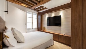 A bedroom with a bed, a TV mounted on the wall, wooden beams on the ceiling, and a window. - 1-Bedroom-Louvre-Saint-Honoré-Palais-Royal-AC (Paris)