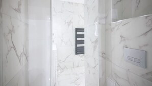 Un baño moderno con paredes de mármol, zona de ducha y panel de control.