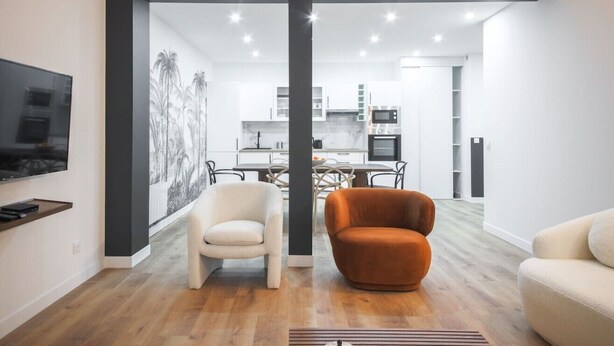 Una sala de estar moderna con televisor, dos sillones y una cocina al fondo.