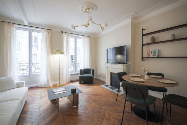 Una sala de estar con un sofá, una mesa de centro, una chimenea, un televisor y una mesa de comedor con sillas.