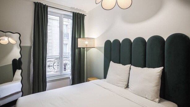 Una camera d'albergo con un letto, una finestra con tende, una lampada e uno specchio.