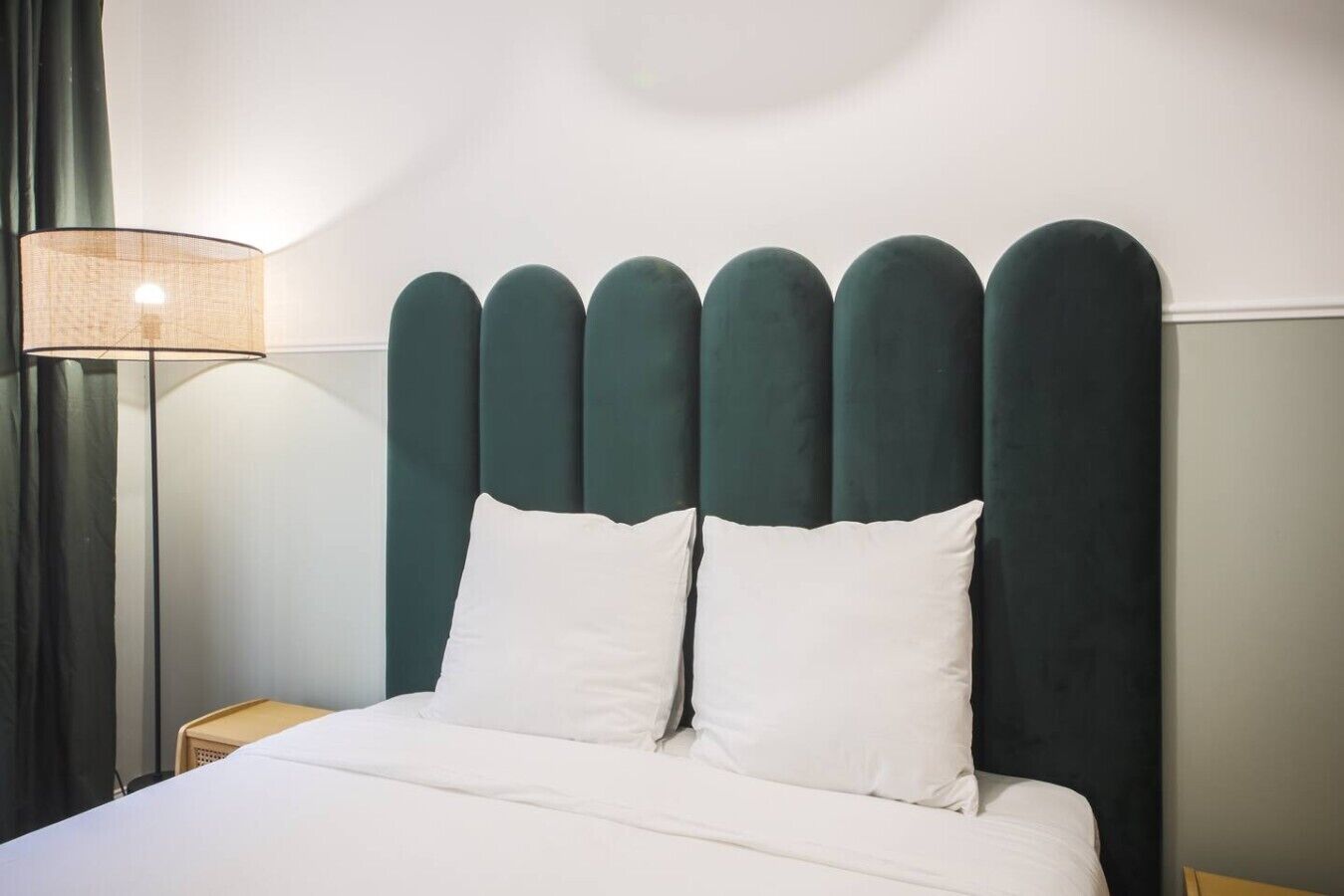 Un lit avec une literie blanche, une tête de lit rembourrée de couleur vert foncé et une lampe de chevet.