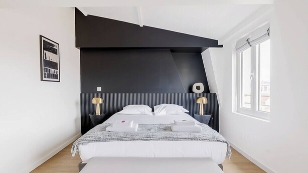 Ein modernes Schlafzimmer mit Bett, Nachttischlampen, einer Bank und einem Fenster.