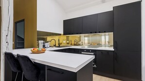 Eine moderne Küche mit schwarzen Schränken, einer weißen Arbeitsplatte und einem eingebauten Backofen. An der Kochinsel stehen zwei schwarze Stühle.