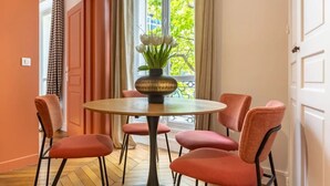 En matplats med ett runt bord, fyra stolar, en vas med blommor och utsikt över grönskan utanför.