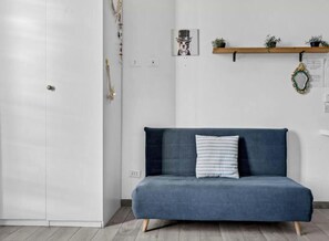 A room with a dark blue sofa, a white door, a wooden shelf with plants, and a framed picture on the wall. - Exclusive Home Brenta: The Duomo in 10 minutes (Milano)